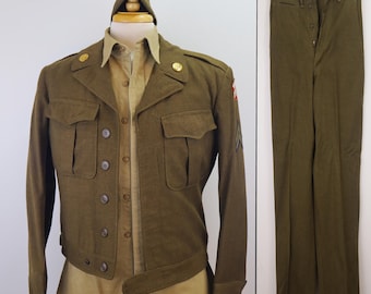 May include: Olive green military uniform consisting of a jacket, shirt, pants, and cap. The jacket has two chest pockets, button closures, and gold-colored buttons. The shirt is tan, and the pants are olive green. The cap is olive green.