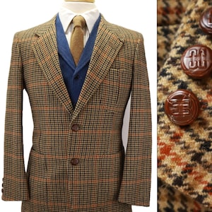 May include: A brown, black, and orange houndstooth blazer featuring a two-button front closure, notched lapels, and a chest pocket. The blazer is layered over a blue vest, a white collared shirt, and a tan tie. Brown buttons feature a logo.