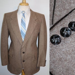 May include: A brown tweed blazer with a herringbone pattern. The blazer has a single button closure and two flap pockets. The blazer has brown buttons with a white cross design.