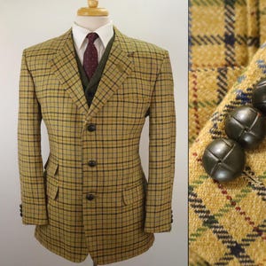 May include: A yellow and black plaid blazer with a matching vest and a white collared shirt. The blazer has three black buttons and two front pockets. The vest is a dark green color, and the tie is a burgundy color.