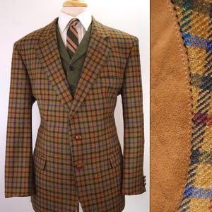 May include: A brown plaid blazer with blue and red accents, featuring suede elbow patches, worn over a green vest, a white collared shirt, and a striped tie. The blazer has two front buttons and two flap pockets on the front of the garment.