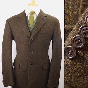May include: A dark olive green tweed blazer with a three-button front closure, notched lapels, and two flap pockets. The blazer is worn over a white collared shirt, a green herringbone vest, and a green tie. A detail view shows four brown buttons.