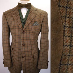 May include: A brown tweed blazer with a plaid pattern, paired with a green vest and a matching bow tie. The blazer has three buttons and a pocket square. The suit is displayed on a mannequin.