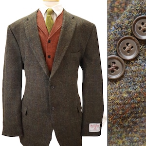 May include: A dark olive green tweed blazer with a two-button closure, worn over a rust-colored waistcoat and a white collared shirt with a green tie. The blazer features a Harris Tweed label on the cuff and brown buttons on the sleeve.