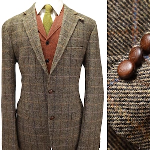 May include: A brown and olive green tweed blazer with a windowpane check pattern, featuring two front buttons and a notched lapel. Underneath is a rust-colored waistcoat with three buttons, a white collared shirt, and a textured olive green necktie.