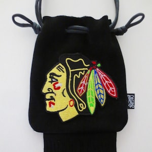 May include: Black drawstring bag with a black fringe. The bag features an embroidered patch of the Chicago Blackhawks logo, which includes a Native American head with a feathered headdress.