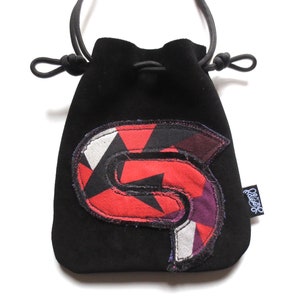 May include: Black velvet drawstring bag with a red, white, and black geometric patch. The patch is shaped like a letter "S" and has a blue outline.