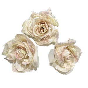 May include: Three artificial rose blossoms in shades of cream, pale pink, and soft green. Each flower features layered, delicate petals with a subtle sheen, arranged in a full, blooming circular shape with a naturalistic appearance.