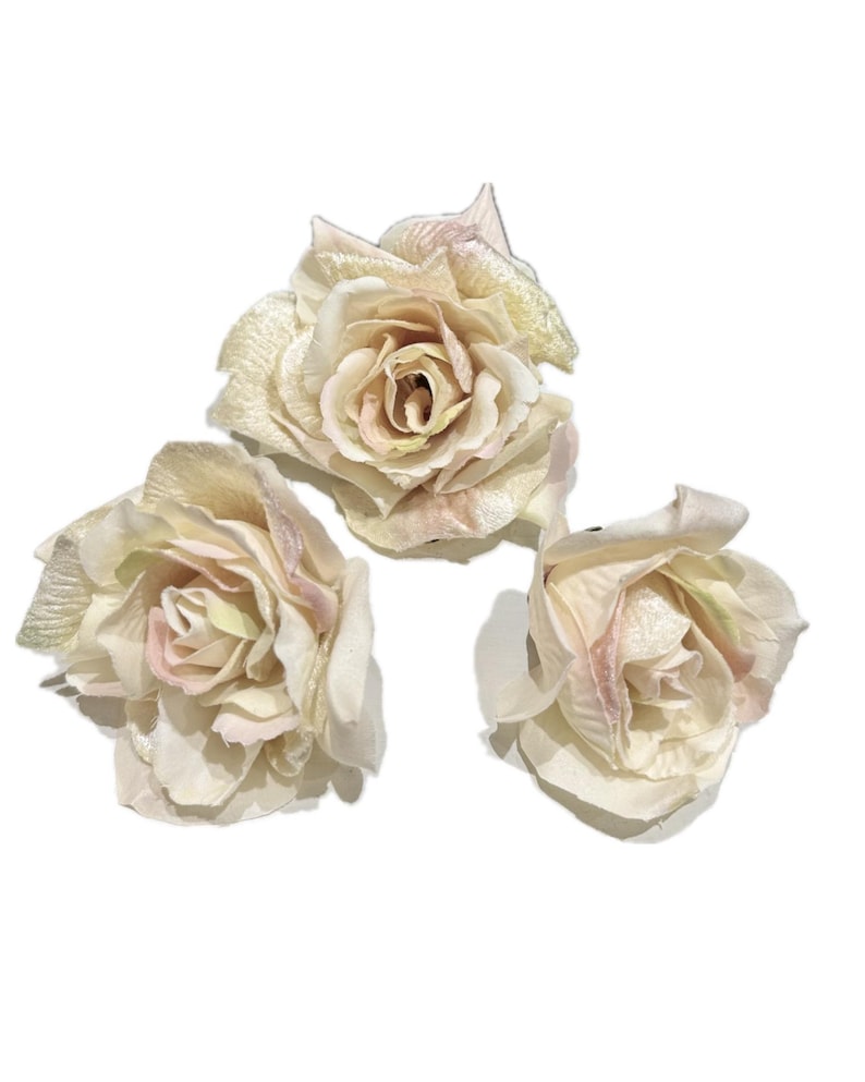 May include: Three artificial rose blossoms in shades of cream, pale pink, and soft green. Each flower features layered, delicate petals with a subtle sheen, arranged in a full, blooming circular shape with a naturalistic appearance.