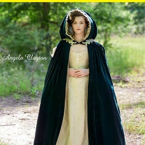 May include: A green velvet hooded cape with gold trim and a gold belt. The cape is worn over a cream-colored dress. The model is standing in a forest setting. McCall's Costumes M7886.