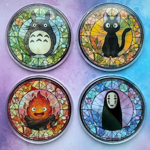 May include: Four circular coasters featuring stained glass style illustrations of animated characters. The top left shows a grey creature, the top right a black cat, the bottom left a fire spirit, and the bottom right a white-masked figure.