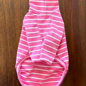 May include: Pink and white striped turtleneck sweater for a small dog. The sweater has a close-fitting turtleneck and long sleeves.