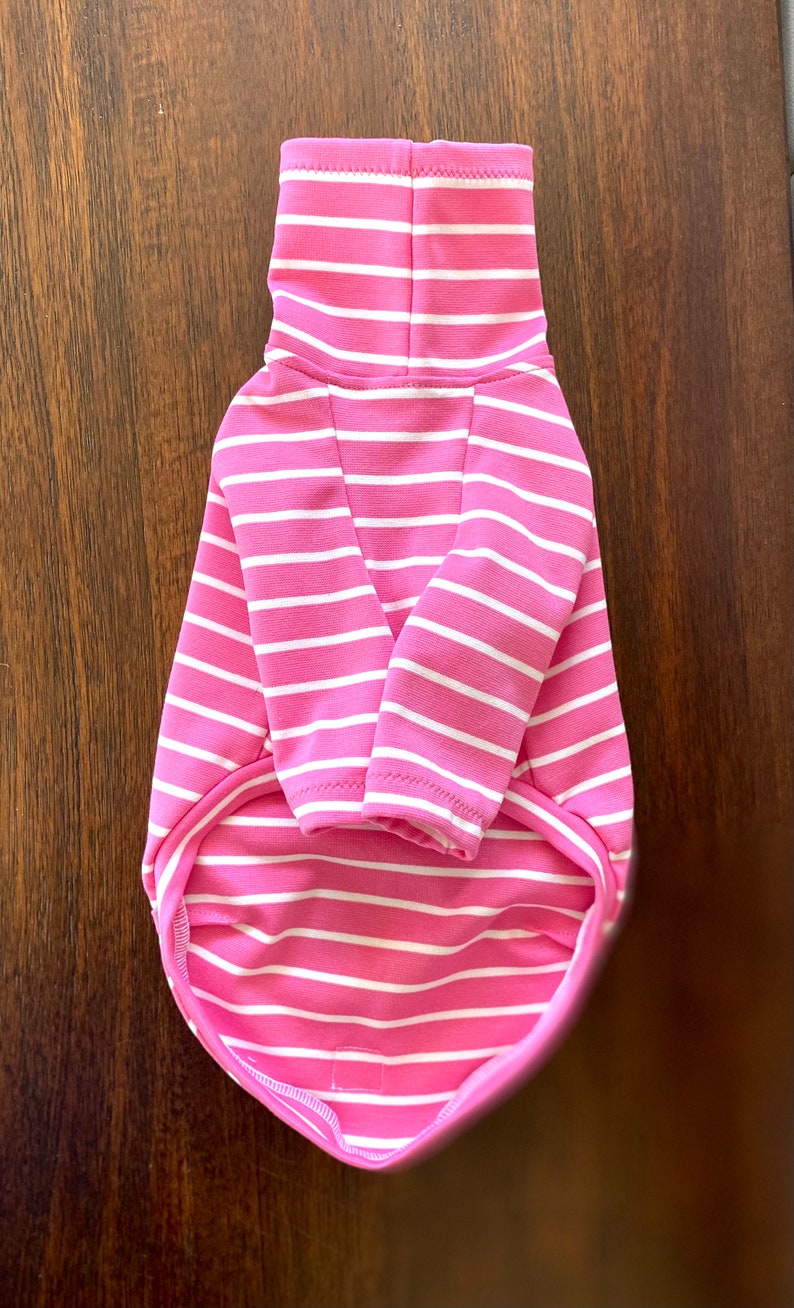 May include: Pink and white striped turtleneck sweater for a small dog. The sweater has a close-fitting turtleneck and long sleeves.