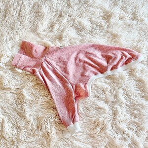 May include: A pink and white dog shirt with a ribbed texture. The shirt has a white trim around the neck and sleeves.