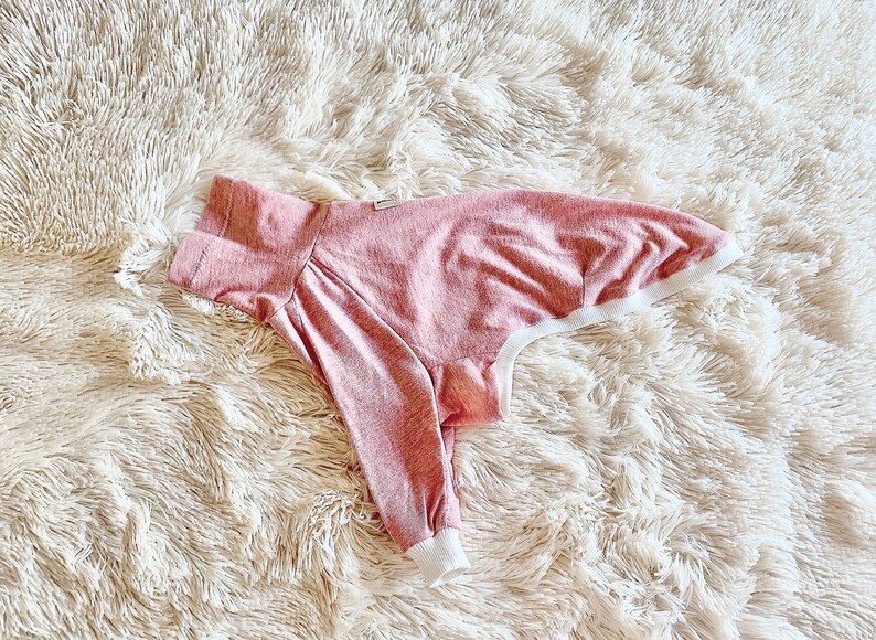 May include: A pink and white dog shirt with a ribbed texture. The shirt has a white trim around the neck and sleeves.