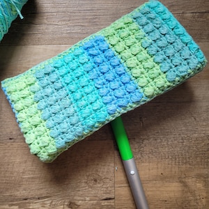 May include: A green, blue, and light blue crocheted mop head attached to a silver and green mop handle.