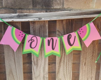 May include: Pink and green watermelon themed banner with the word "one" in black cursive lettering.