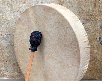 May include: A large, round, beige drum with a wooden stick and a black and floral patterned head.