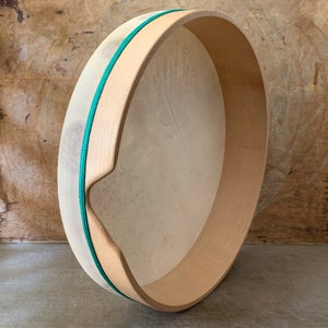 May include: A wooden frame drum with a natural colored skin and a green rope around the edge.
