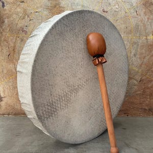 May include: A white drum with a brown leather mallet. The drum is made of wood and has a natural finish. The mallet has a leather head and a wooden handle.