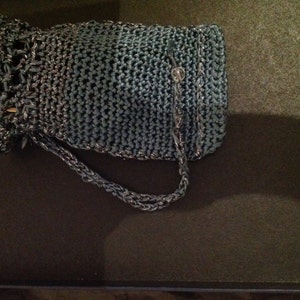 Grey crochet clutch bag from an alternate angle, showing the drawstring-style closure and strap.