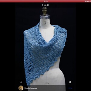 May include: A light blue triangular shawl featuring an openwork crochet pattern with a scalloped edge. The garment is draped over a white dress form, showcasing the intricate, airy texture of the yarn and the asymmetrical drape of the fabric.