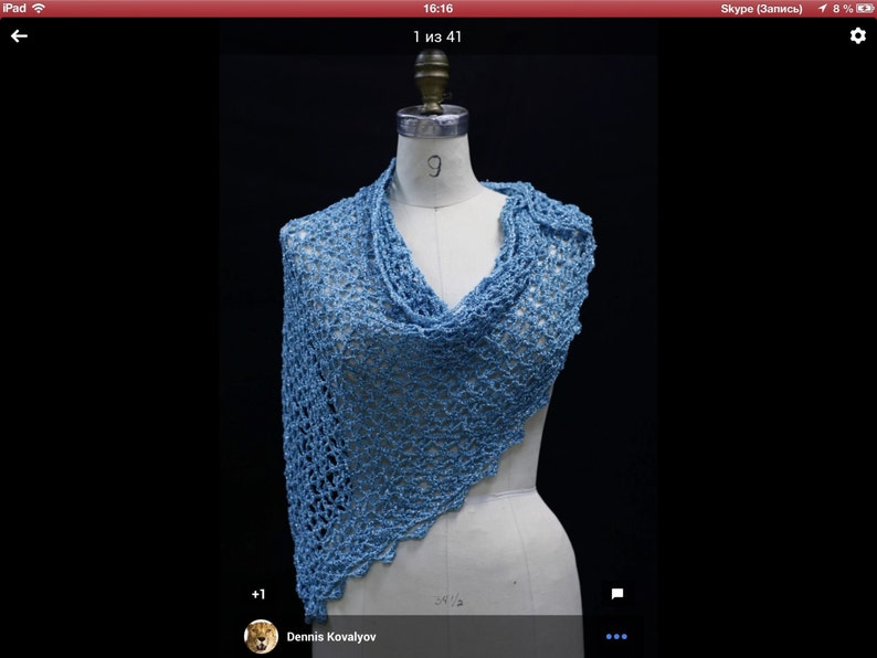 May include: A light blue triangular shawl featuring an openwork crochet pattern with a scalloped edge. The garment is draped over a white dress form, showcasing the intricate, airy texture of the yarn and the asymmetrical drape of the fabric.