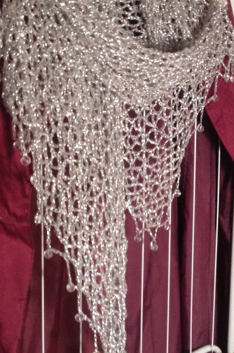 Close-up of the silver lurex shawl over a burgundy garment, showing the beaded edge and openwork crochet.