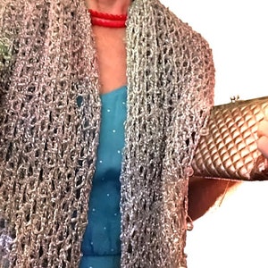 Woman wearing a silver lurex crochet shawl over a turquoise dress with a red necklace, holding a metallic clutch as the wrap frames her shoulders.