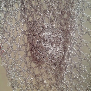 Close-up of a crocheted flower motif on the silver lurex shawl, showing the layered petals and fine stitches.