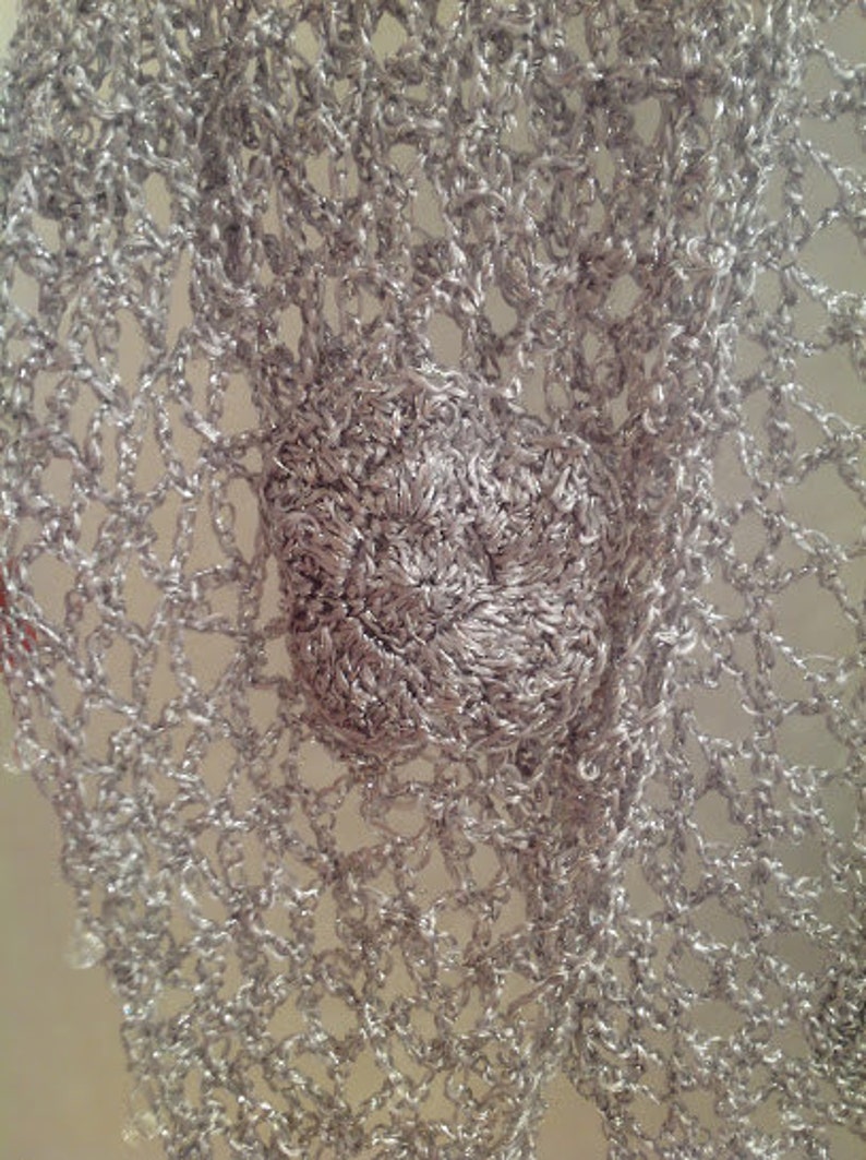 Close-up of a crocheted flower motif on the silver lurex shawl, showing the layered petals and fine stitches.