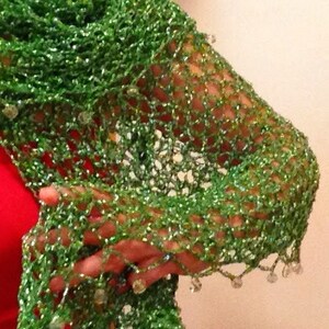 Green lurex shawl wrapped around the shoulders over a red dress, side view of the beaded openwork with a straw hat above.