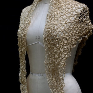 Gold beaded crochet shawl draped over a dress-form mannequin, front view of the shimmering wrap against a dark background.