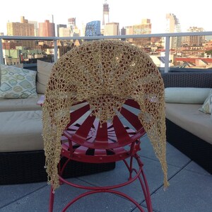Gold shawl draped over a red metal chair on a rooftop terrace, NYC skyline and outdoor lounge seating in the background.