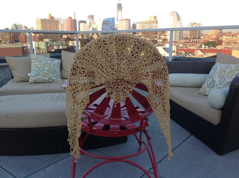 Gold shawl draped over a red metal chair on a rooftop terrace, NYC skyline and outdoor lounge seating in the background.