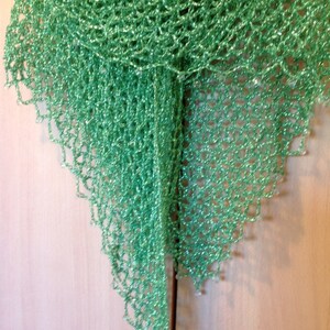 Green shawl on a wooden door, alternate view of the openwork drape and shimmering weave.