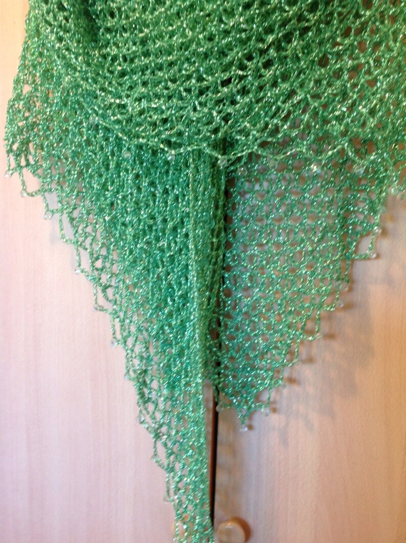 Green shawl on a wooden door, alternate view of the openwork drape and shimmering weave.