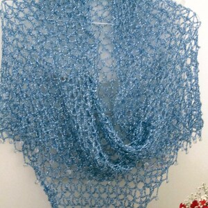 Sky blue shawl on a hanger folded into a soft cowl, red flowers arranged below.
