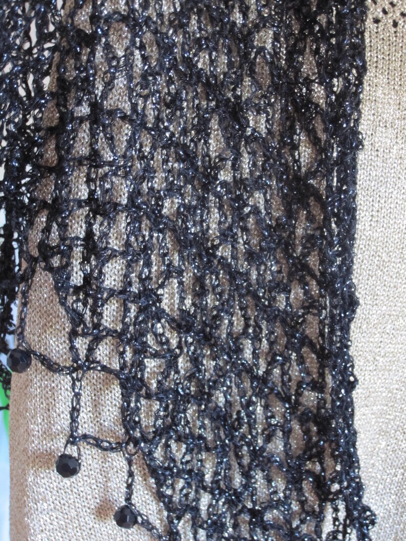Close-up of the black lurex crochet, revealing tight stitches and dark beads hanging from the edge.