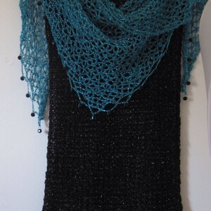 Turquoise shawl draped over a black fringed dress on a hanger, front view of the openwork wrap.