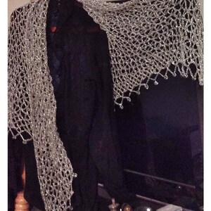 Silver beaded shawl draped over a black garment, side view highlighting its long, flowing openwork drape.