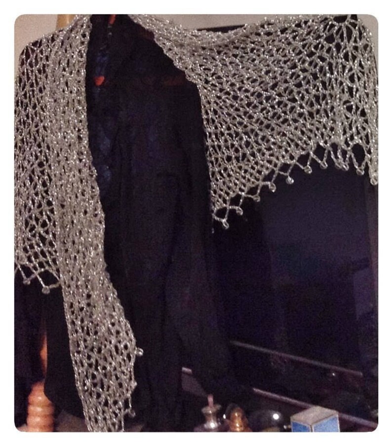 Silver beaded shawl draped over a black garment, side view highlighting its long, flowing openwork drape.