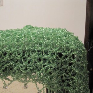 Green shawl draped over a dark surface, showing the beaded edge and airy crochet pattern.