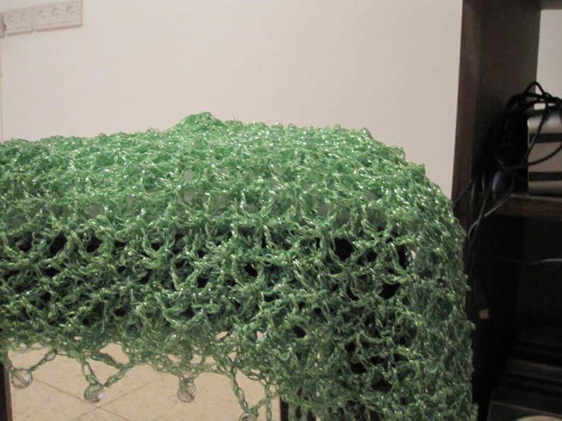 Green shawl draped over a dark surface, showing the beaded edge and airy crochet pattern.