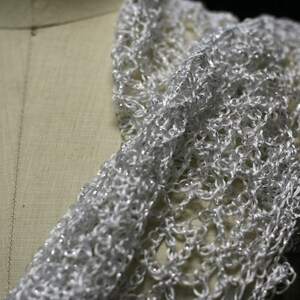 Close-up of the white lurex crochet on the mannequin's shoulder, fine stitches and subtle sheen.