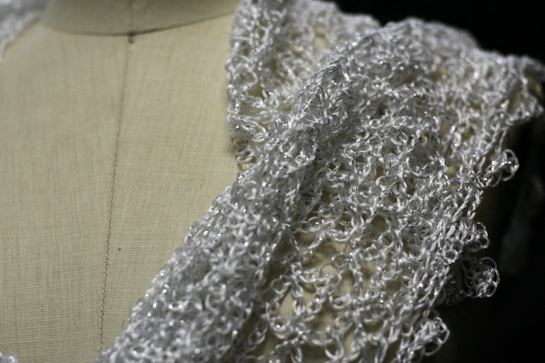 Close-up of the white lurex crochet on the mannequin's shoulder, fine stitches and subtle sheen.