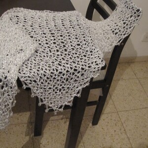May include: A white triangular shawl featuring an openwork crochet pattern with a shimmering, metallic finish. The edges of the shawl are adorned with small, clear, dangling beads that hang from the points of the intricate, lacy knit structure.