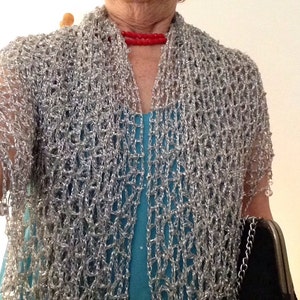Silver lurex crochet shawl draped like a cape over a turquoise dress and red necklace, front view of the sparkling openwork.