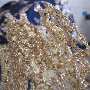 Close-up of the champagne lurex crochet texture, golden stitches glowing in the light.