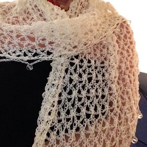 May include: A white crocheted shawl featuring an open, airy lattice stitch pattern. The edges of the shawl are finished with small, clear, spherical beads attached at regular intervals along the border, creating a delicate, textured appearance.